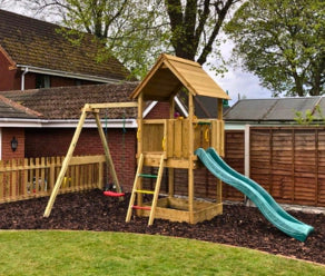 Parque infantil de madera con tobogán y columpio instalado en un jardín